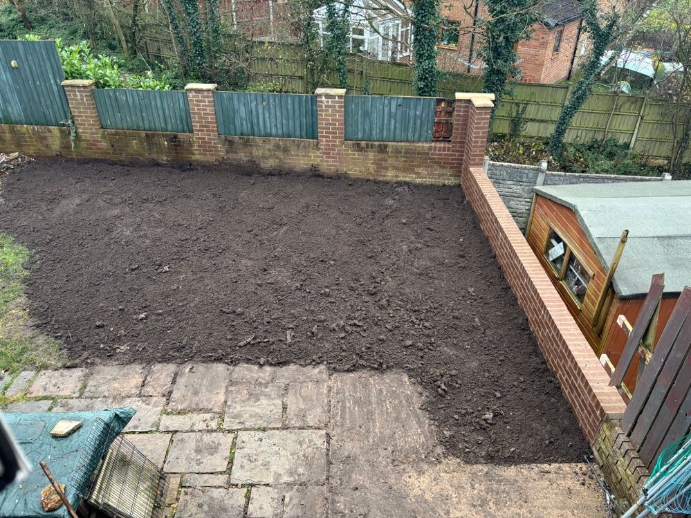 The rebuilt brick retaining wall with new fencing and the ground regraded ready for turf